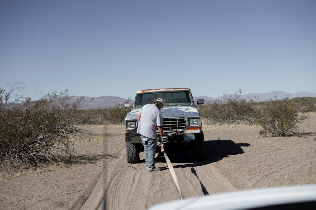 Man assisting stranded pickup truck in arid desert setting.